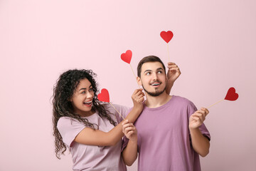 Wall Mural - Funny young couple with paper hearts for Valentine's day on pink background