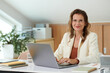 © DragonImages - Portrait of cheerful successful female entrepreneur working on laptop in home office