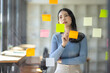 © David - Happy asian businesswoman planning new project with sticky note in a creative writing on blank office glass