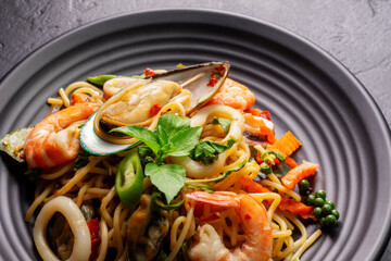 Wall Mural - Close-up of drunken spaghetti with seafood with shrimp, squid, clams, chili, and basil. Healthy Thai Asian food in a plate on a black background table.