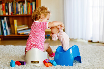 Closeup of cute little 12 months old toddler baby girl child sitting on potty. Kid playing with doll toy. Toilet training concept. Baby learning, development steps