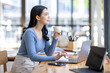 © David - Beautiful young smiling Asian businesswoman working on laptop and drinking coffee, Asia businesswoman working document finance and calculator in her office.