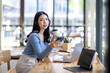 © David - Beautiful young smiling Asian businesswoman working on laptop and drinking coffee, Asia businesswoman working document finance and calculator in her office.