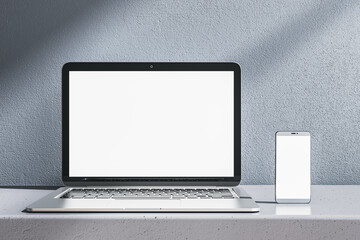 Poster - Close up of empty white laptop and smartphone on gray desk. Concrete wall background. Device presentation and online education concept. Mock up, 3D Rendering.