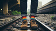 Man standing on train track, low angle closeup detail on his shoes and socks in the colors of the rainbow, above ground.