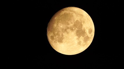Wall Mural - A glowing golden huge full moon seen from earth through the atmosphere against a starry night sky. A large full moon moves across the sky, the moon moving from the bottom left frame to the top right.
