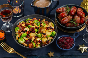 Wall Mural - Roasted brussel sprouts with bacon, cashew and cranberry and pigs in blankets for festive Christmas dinner. Dark blue background