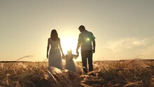 Silhouette Of Mother With Father Holding Hands Of Funny Daughter Jumping Over Grass. Wife And Husband Walk Looking At Daughter Strolling And Jumping. Mother With Father Walking At Sunset On Field