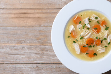 Wall Mural - Chicken soup with vegetables on wooden table. Top view. Copy space