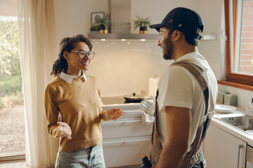 Wall Mural - Beautiful young woman talking to male handyman while standing at the kitchen at home