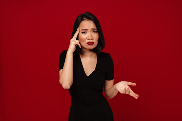 Wall Mural - Annoyed asian woman rubbing her temple and gesturing isolated over red background