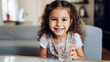 Portrait of cheerful pretty little girl sitting on couch at home holding glass of water. Hydration, children healthy lifestyle