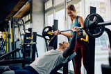 Fototapeta  - Happy athletic couple exercising with barbel in gym.
