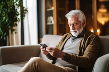 Senior Man Relaxed And Happy Using The Mobile Phone Sitting On The Sofa At Home. Concept Of Technology And Older People.