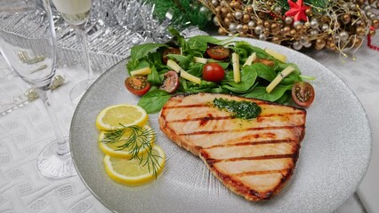 Sticker - Grilled swordfish steak with fresh salad, tomatoes and cheese on a plate rotating. Christmas New Year decoration. Pour champagne into a glass. Close up