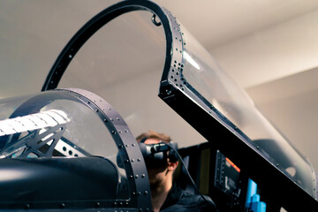 Wall Mural - boy sitting in flight simulator of military plane wearing virtual reality glasses during flight entertainment