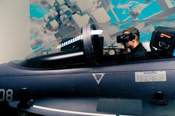 Wall Mural - boy sitting in flight simulator of military plane wearing virtual reality glasses during flight entertainment