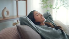 Relaxed young asian woman falling on comfortable sofa at home, female enjoying carefree peaceful weekend relaxation time alone in living room.