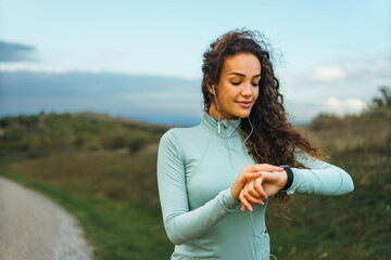 A fitness girl is looking at her smart watch to see how many steps she has been taking, as well as her pulse rate.