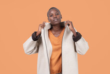 Portrait Of Young Bold African American Female In Long Zipper Coat Confidently Looking At Camera Standing On Orange Background