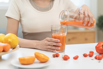 Detox juice concept, hand of woman holding bottle making carrot, vegetable smoothie pouring in glass for diet at home, female drinking healthy meal food for weight loss. Lifestyle vegan nutrition.