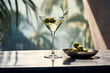 © Ivan - Green olives in martini glass on table with palm tree background