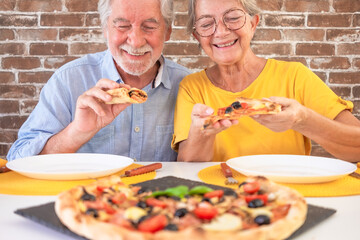 Wall Mural - Happy senior couple ready to bite a slice of pizza. Elderly woman and man share a traditional Italian pizza for dinner