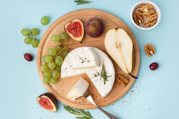 Wall Mural - Wooden board with pieces of tasty Camembert cheese, nuts and fruits on blue background