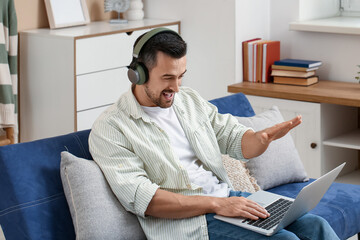 Sticker - Handsome man with headphones and laptop video chatting on sofa in living room