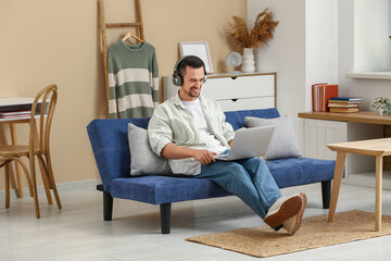 Poster - Handsome man with headphones using laptop on sofa in living room