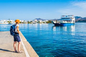 Wall Mural - Youung woman tourist with backpack looking at ferry from Kimolos arriving in Pollonia port, Milos island, Cyclades, Greece