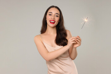 Sticker - Christmas celebration. Beautiful young woman with sparkler on grey background