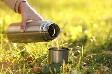 Sticker - Woman pouring tea from thermos into cup lid on green grass outdoors, closeup. Space for text