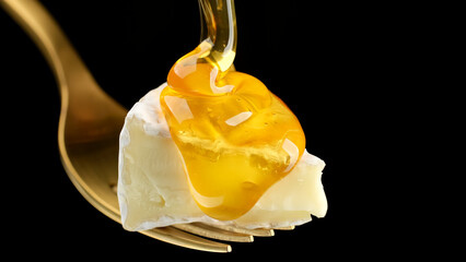 Wall Mural - Thick honey pouring on pieces of cheese, macro. Camembert or brie cheese with honey, isolated on black background