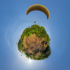 Wall Mural - green grass little planet in blue sky with yellow paragliding parachute