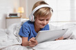 © New Africa - Cute little boy with headphones and tablet listening to audiobook in bed at home