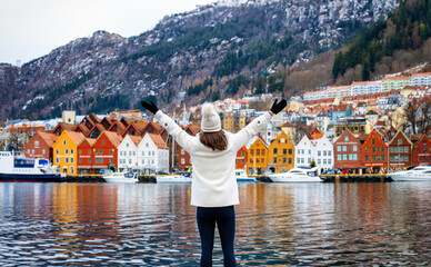 Wall Mural - A happy tourist woman enjoys the beautiful view of the Bryggen district in Bergen, Norway, during a cold winter day with snow