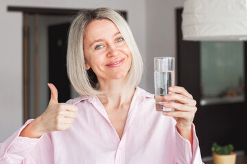 Poster - adult woman holding glass of pure mineral water at home