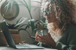 One serene woman with curly hair look on laptop display and drink coffee or tea. Modern healthy people working at home with green gardens indoor plants in background. Green mood color people lifestyle