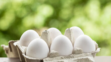 Close Up View Of Half A Dozen White Eggs In A Bowl Or Egg Cup With Selective Focus And Out Of Focus Natural Background For Copy Space. Dozen White Eggs In A Cardboard Egg Cup With A Green Background.