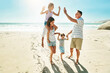 © GR/peopleimages.com - Parents, children and beach for high five happy or summer travel vacation, ocean sunshine or family development. Man, woman and kids on sand for holiday relax walking or outdoor, clean air or smile