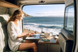 Independent woman sitting inside a camper van in using a laptop. Living and working inside camper van vehicle in travel and digital nomad free lifestyle. 