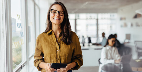 Poster - Happy business woman holding a tablet while standing in an office