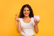 © Prostock-studio - Emotional young woman with piggybank and coin on yellow