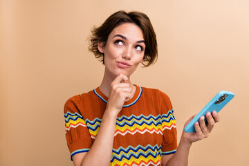 Poster - Photo of pretty minded girl hand touch chin hold smart phone look empty space isolated on beige color background