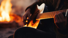 Close-up Of An Acoustic Guitar In A Musician's Lap, Blurred Background Of A Bonfire