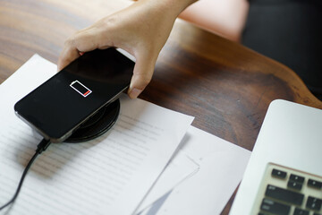 Wall Mural - Charging mobile phone battery with wireless charging device in the table. Smartphone charging on a charging pad. Mobile phone near wireless charger Modern lifestyle technology concept