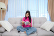 © เลิศลักษณ์ ทิพชัย - Asian teenage girl Reading a book at her home on the cloth sofa in the living room with a nice holiday at home.