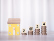 © maybeiii - Miniature house, Wooden blocks with number 2024 on stack of coins. The concept of payment tax for house, Property investment, House mortgage, Real estate in New Year 2024.