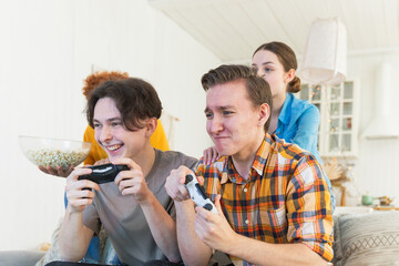 Wall Mural - Home party. Cheerful group of friends playing video games at home. Happy diverse group buddies having fun together indoor. Friendship leisure entertainment concept. Young best friends enjoying weekend